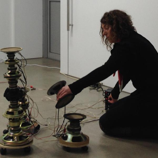 Charlotte kneels on the floor stacking speaker cones on top of each other.