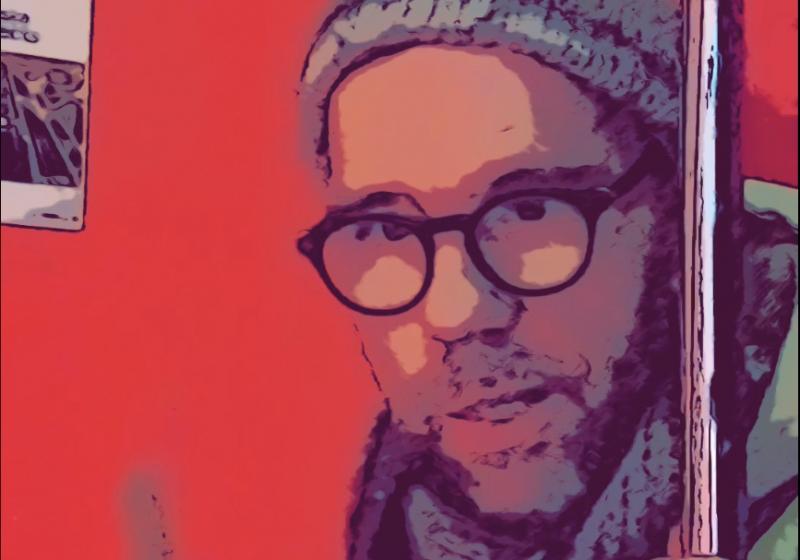 Chris OConnor is wearing a pompom hat and is holding two drum sticks up. He is looking staright down the lens of the camera.