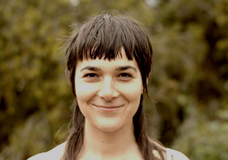 A portrait of Erin looking straight to the camera. There are blurry trees making the entire background green.